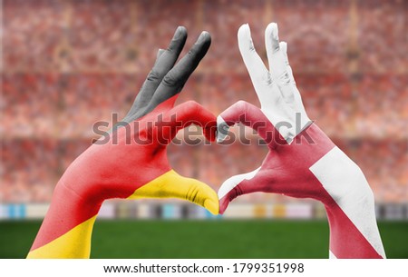 A closeup of two hands with Germany and England flag colors forming a heart inside a soccer field