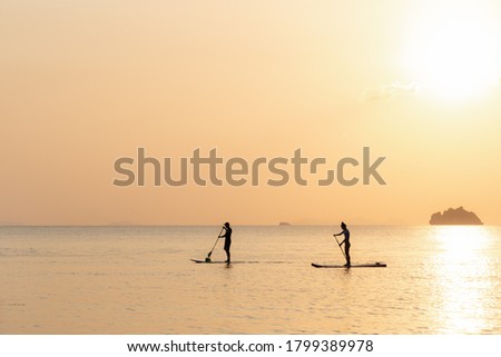Couple swims on paddle boards on the sea against the backdrop of islands and golden sunset