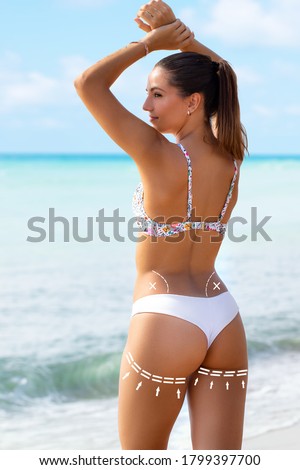 Close up rear view portrait of young woman in white bikini showing perfect muscular buttock. Brunette standing on beach with conceptual surgical dotted contour lines.