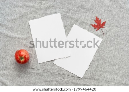 Blank business cards mockup, red apple and dry maple leaf on gray linen textile. Modern minimal stationery scene. Top view, flat lay.