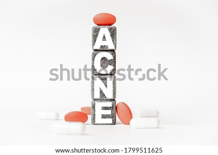 a group of white and red pills and cubes with the word acne on them, white background. Concept carehealth, treatment, therapy.