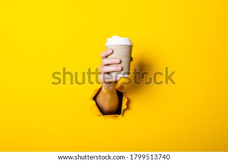 Man's hand holds a paper cup with coffee closed by a bump on a bright yellow background Royalty-Free Stock Photo #1799513740