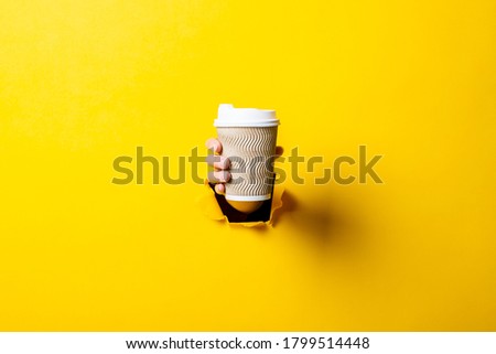 Female hand holding a paper cup of coffee on a bright yellow background.