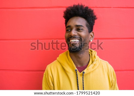 Portrait of young afro american man looking confident and posing against red wall.