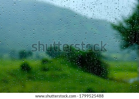 Water droplets on glass and Monsoon Landscape in the background at Purandar near Pune India. Monsoon is the annual rainy season in India from June to September.