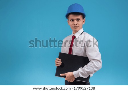 Portrait of young engineer smiling wear protective helmets and holding notebook isolated on blue background