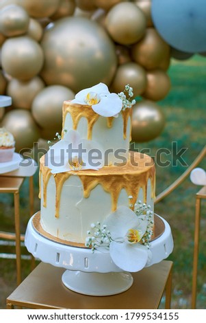 A two-story wedding cake decorated with orchedea flowers. Wedding decoration in gold color, balloon decor.