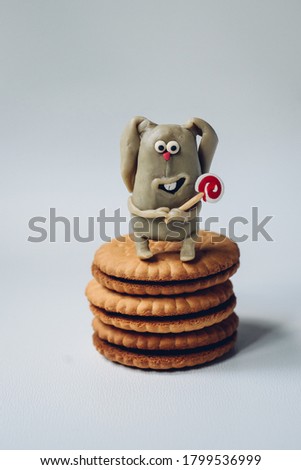 A funny hare stands on a cookie, with a candy in its paws and a wide smile.