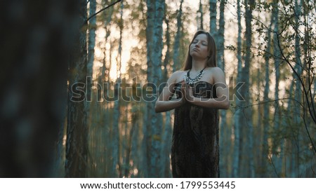 young woman praying with closed eyes in nature during the sunset surrounded by trees. High quality photo