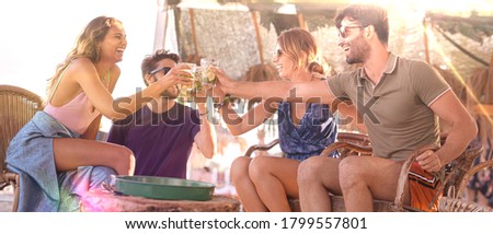 Young best friends drinking at beach cocktail pub - Summer concept with milenials having fun together toasting drinks - Backlight lens flare Royalty-Free Stock Photo #1799557801