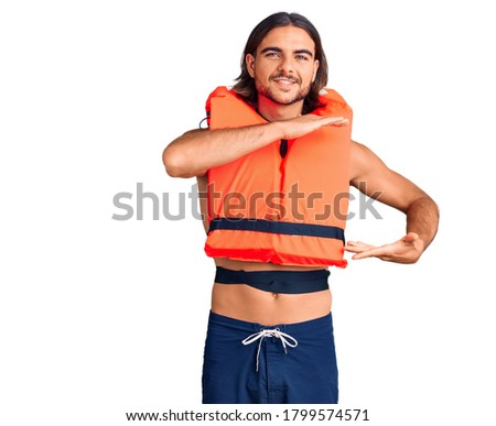 Young handsome man wearing nautical lifejacket gesturing with hands showing big and large size sign, measure symbol. smiling looking at the camera. measuring concept. 