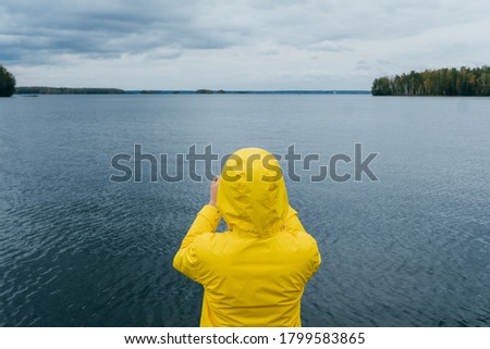 Woman photographing autumn lake on phone
