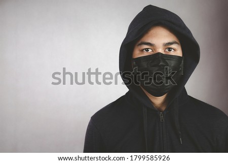An image of a man in a hood or a jig on a dark gray background with a black mask covering his mouth and nose.