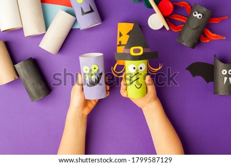 Boy makes Halloween toys from paper. toilet roll tube by hands. Creative DIY for kids on traditional purple backgrpund. Home decor project party. Halloween crafts inspiration, recycle concept