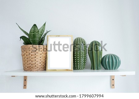 mock-up gold photo frame on a shelf with indoor flower and cacti figurines.
