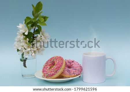 A white mug with a hot drink,donuts on a plate and a sprig of a blossoming apple tree create a romantic mood.photo in pastel colors,on a blue background.Idea-postcard,mockup for advertising on a mug.