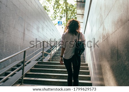 Slender girl in a white shirt with a handbag climbs the stairs from the underpass Royalty-Free Stock Photo #1799629573