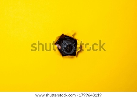 Black professional camera can be seen from a torn yellow cardboard