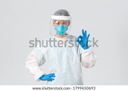 Covid-19, coronavirus disease, healthcare workers concept. Serious-looking professional female asian doctor in personal protective equipment, showing okay gesture, ensure safety of patient