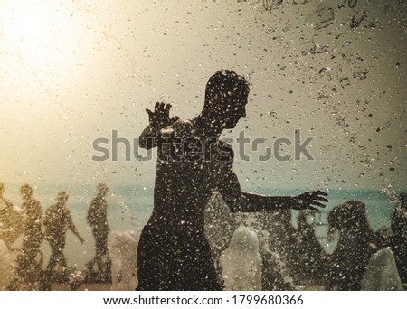the silhouette of a happy man playing in a fountain of water in the light of the setting sun. Gurgling water fountain in the city Park on a hot summer day.