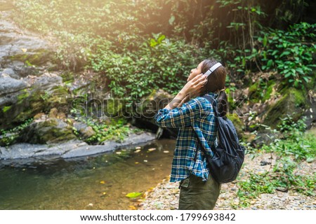 Asian woman tourist traveling adventure summer exploration in nature jungle into forest waterfall using headphone technology listening to music,