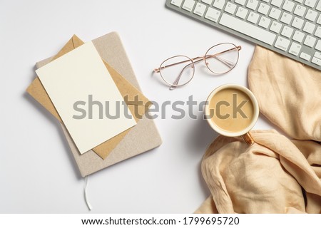 Elegant feminine workspace with pc keyboard, glasses, beige plaid, glasses, blank paper card, envelope, notebook on white background. Flat lay, top view.