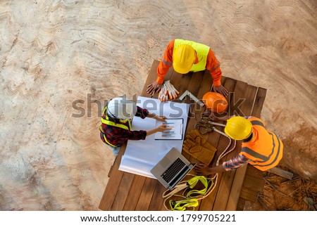 Aerial view of team of engineer and architects meeting and planning measuring layout of building blueprints at construction site.
