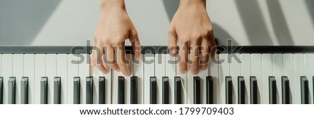 Woman learning to play piano at home on digital keyboard. Panoramic banner crop of hands playing beginner chords to learn playing by herself.