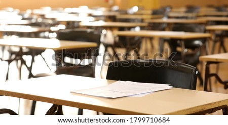 A high school hall or room set up ready for an end of year final exam to be sat by students. examination paper sitting on the edge of a desk or table.  Royalty-Free Stock Photo #1799710684