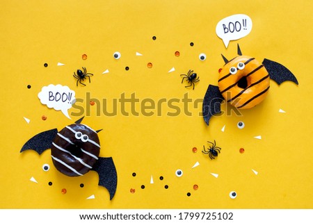 Happy halloween holiday concept. Funny food for kids - scared donuts on bright yellow background as a bat costume with black spider and eyes. Halloween party greeting card. Spelling word Boo