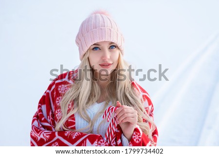 Portrait of a cute woman against the snow in a pink hat and red plaid posing for the camera