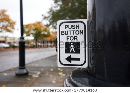 Push button for walk signal sign attached to a post on a city street.