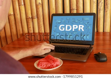GDPR concept, laptop on a table, blue screen. A man works at laptop and hand holding digital tablets sign general data protection regulation. Cybersecurity and information privacy