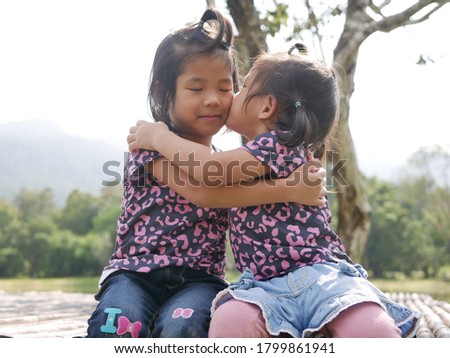 Two little girls, sisters, hugging and kissing on a bench in the evening sunlight - sister bond and love concept.