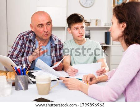 Parents with teenager son reading and writing some documents at home table 

