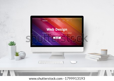 Web design studio concept with computer on work desk and company web site on display. White wooden desk with keyboard, mose, plants and books