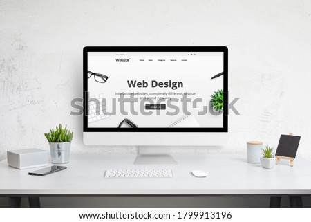 Web design company web site concept on computer display. Modern flat design website. Office desk with plants, phone, keyboard and mouse. Royalty-Free Stock Photo #1799913196