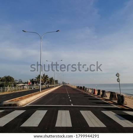 A long road in Seberang Takir, Terengganu, Malaysia during sunny day. A beautiful sea by the road that can be viewed and enjoyed by people who drive there. A blue sky and white clouds as backgrounds. 