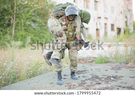 A military man carries his wounded partner during combat operations. A soldier's friend saves his comrade. Patriotism, loyalty, bravery. An accident during the war. Royalty-Free Stock Photo #1799955472