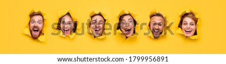 Group of excited hilarious young people with amazed faces looking through ripped holes in bright yellow paper