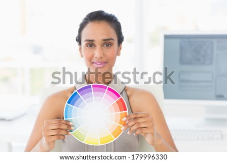 Designer at her desk showing colour wheel to camera in creative office
