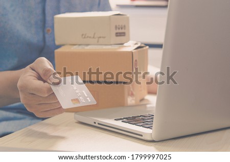 Man hands are holding a credit card and a box parcel hematite and laptop at the table.Online delivery service business concept.