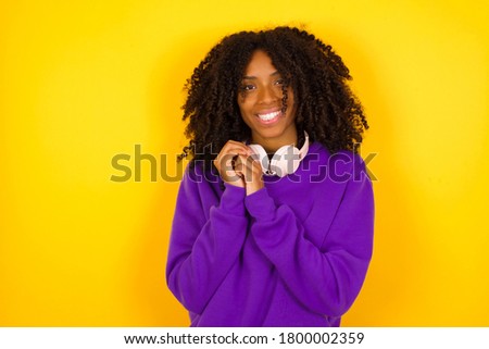 Dreamy charming young female with pleasant expression, keeps hands crossed near face, excited about something pleasant, poses against gray background.