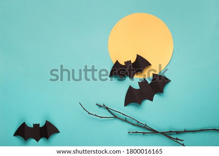 Halloween paper decorations on blue background. Black bats, tree branch and moon. Halloween concept. Flat lay, top view, overhead. Minimal style. Halloween party greeting card mockup with copy space. 