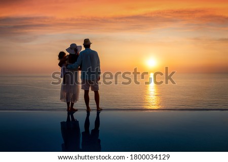 A hugging family on summer holidays enjoys the beautiful sunset over the sea by the swimming pool
