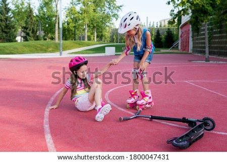 Kids learning to skating in park. Girl  with roller skates helping friend to stand up. Children playing outside. Active healthy leisure and outdoor sport for kids