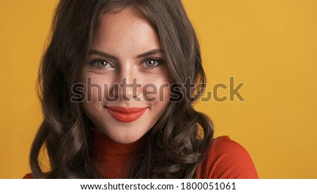 Portrait of cute brunette girl with red lips charmingly looking in camera over colorful background  