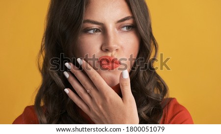 Portrait of thoughtful brunette girl correcting lipstick over yellow background