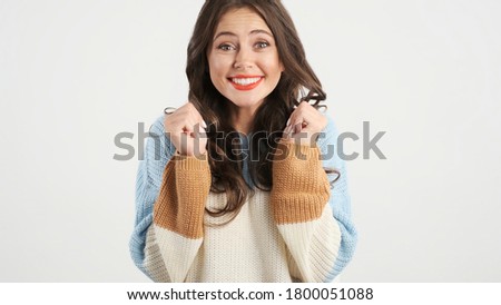 Beautiful excited brunette girl in cozy sweater happily posing on camera over white background