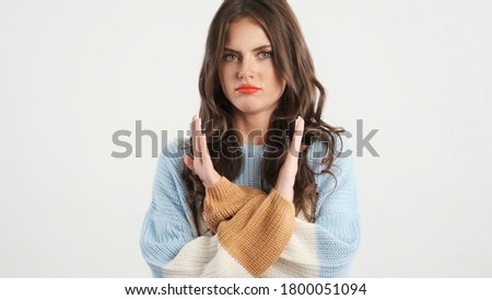 Attractive serious brunette girl in sweater showing no gesture with crossed hands on camera over white background